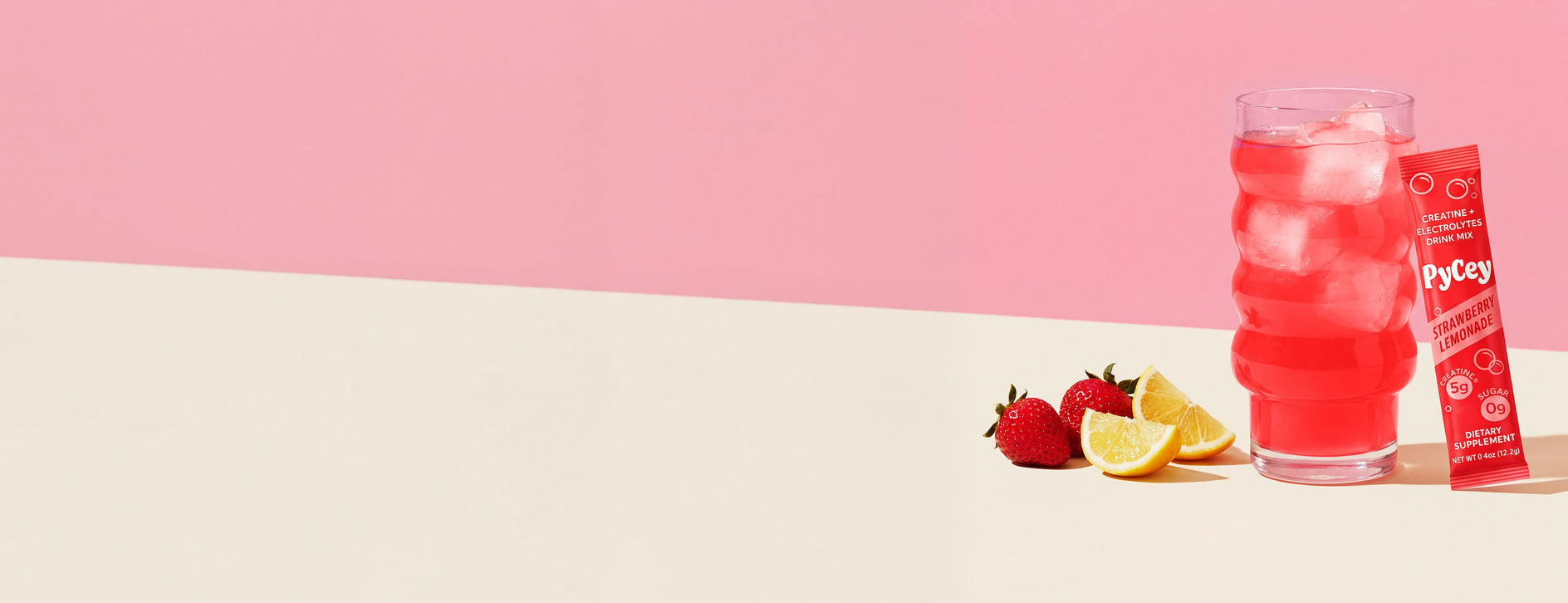 Glass of Pycey Strawberry lemonade with ice and strawberries on a white surface with a pink background