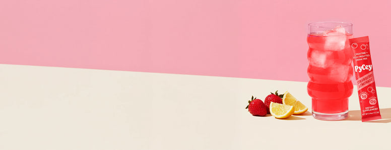 Glass of Pycey Strawberry lemonade with ice and strawberries on a white surface with a pink background